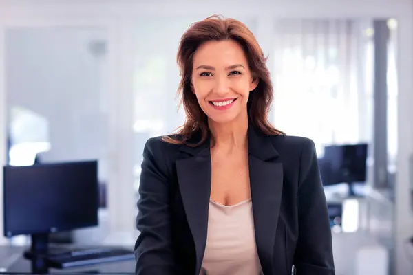 ブルネットはオフィスに座って陽気な笑顔で年をとったビジネスマン ビジネスカジュアルを身に着けている自信のあるプロフェッショナル女性 ロイヤリティフリーのストック画像