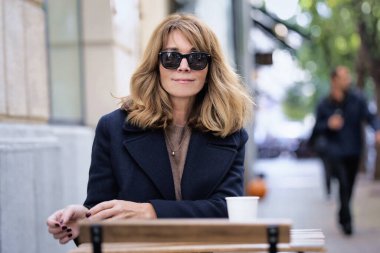 Sokakta elinde bir fincan kahve olan orta yaşlı bir kadın.