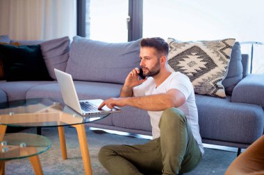 Laptop ve akıllı telefon kullanan orta yaşlı bir adam. Evden çalışan kendine güvenen bir erkek. Merkez Ofis.