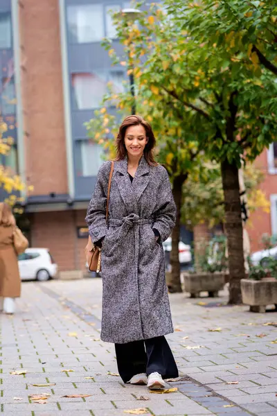 秋天的一天 一个头发乌黑的中年妇女走在城市街道上 她穿着粗花呢外套 免版税图库照片