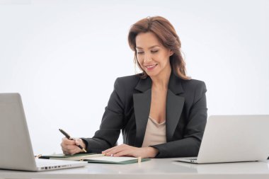 Orta yaşlı bir iş kadını soyutlanmış bir geçmişe karşı masa başında oturuyor. İş için dizüstü bilgisayar kullanan kendine güvenen profesyonel bir kadın. Boşluğu kopyala.