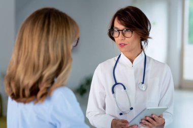 Ofiste çalışan ve semptomlarını açıklayıp danışmanlık yaparken hastayı dinleyen kadın doktor..