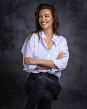 Esmer bir kadının stüdyo portresi izole edilmiş arka planda oturuyor. Tişört giyen ve neşeli gülümseyen çekici bir kadın. Boşluğu kopyala. 