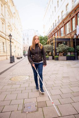 Sokakta yürüyen beyaz bastonlu kör kadın. Sıradan kıyafetler giyen ve bastonuyla sokakta yürüyen görme engelli bir kadın. Tam boy çekim.