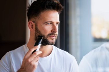 Evde elektrikli tıraş makinesi kullanan orta yaşlı yakışıklı bir adamın portresi.. 