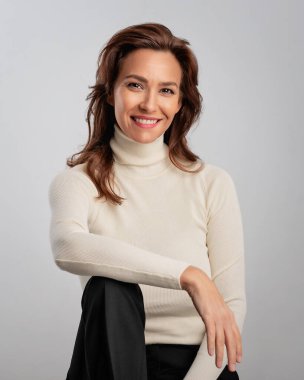 Esmer saçlı, balıkçı yaka kazak giyen ve izole edilmiş beyaz arka plana gülümseyen bir kadının stüdyo portresi. Boşluğu kopyala. 