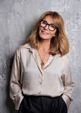 Gri bir duvarın önünde duran çekici sarı saçlı kadın. Gömlek ve pantolon giyen ve kameraya bakan gülümseyen bir kadın. Boşluğu kopyala.