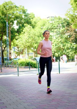 Şehirde koşan uzun boylu genç bir kadın. Esmer, kadın, spor giyiniyor. Tam boy çekim.
