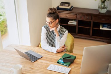 Evde dizüstü bilgisayarının başında oturan ve çalışan genç bir kadın. Evde çalışan kendine güvenen bir kadın. Merkez Ofis.