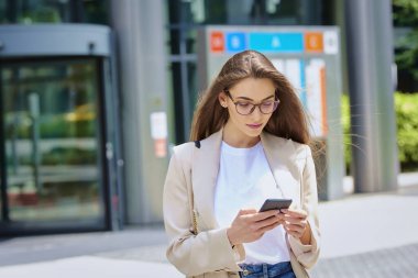 Esmer, kadın, şehirde yürürken akıllı telefonuna bakıyor. Kendine güveni tam bir iş kadını.. 