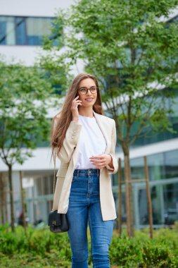 Şehirde yürürken akıllı telefonuna gülümseyen bir kadın. Esmer saçlı iş kadını telefonda biriyle konuşuyor.. 