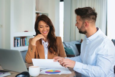 Yeni bir proje üzerinde çalışırken bilgisayarla gülümseyen iş adamları. Çekici bir iş kadını masada oturuyor ve orta yaşlı bir iş adamı yanında oturuyor ve.... 