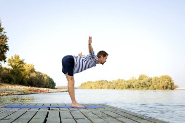 Kafkasyalı bir adam göl kenarındaki iskelede yoga yapıyor.. 