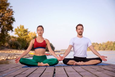 Gün batımında plajda yoga yapan genç bir çift. Tam boy çekim.
