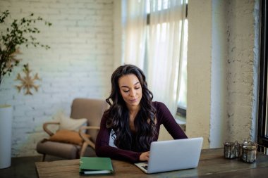 Pencerenin yanındaki masada oturan ve dizüstü bilgisayarı üzerinde çalışan Afro-Amerikalı bir kadın. Merkez ofis. Sıradan kıyafetler giyen çekici bir kadın.. 