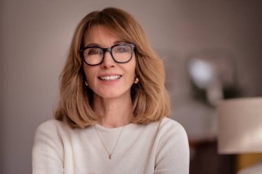 Sarı saçlı olgun bir kadının yakın plan portresi. Kameraya bakıyor ve gülümsüyor.. 