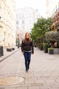 Sokakta yürüyen beyaz bastonlu kör kadın. Görme engelli bir kadın günlük kıyafetler giyiyor ve bastonuyla sokakta yürüyor.. 