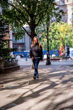 Sokakta yürüyen beyaz bastonlu kör kadın. Görme engelli bir kadın günlük kıyafetler giyiyor ve bastonuyla sokakta yürüyor.. 