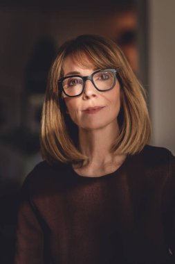 Samimi dairesinde duran gülümseyen kadının portresi. Süveter ve gözlük takan orta yaşlı kadın..