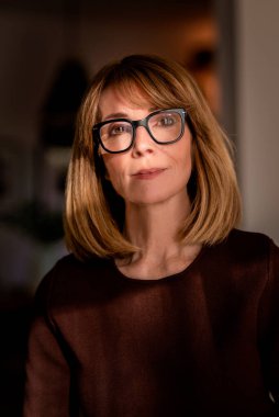 Samimi dairesinde duran gülümseyen kadının portresi. Süveter ve gözlük takan orta yaşlı kadın..