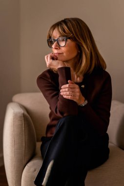 Gülümseyen sarı saçlı kadın duvarın önünde rahatlıyor ve düşünceli görünüyor. Günlük kıyafetler giyen beyaz bir kadın..