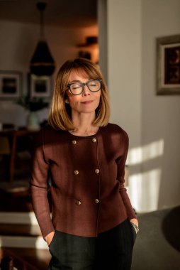 Sarı saçlı, gözleri kapalı bir kadın pencerenin yanında duruyor. 