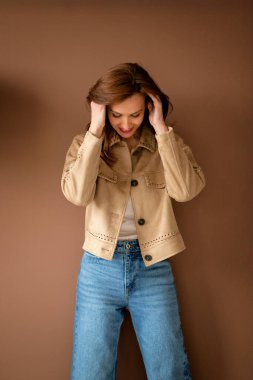 Kahverengi duvarda duran esmer, çekici bir kadının portresi. Ceket ve kot pantolon giyen orta yaşlı bir kadın. Boşluğu kopyala. 