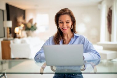 Esmer kadın masada oturuyor ve laptopunu iş için kullanıyor. Evden çalışan çekici bir kadın. Merkez Ofis.  