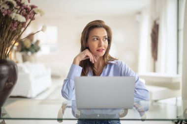 Esmer kadın masada oturuyor ve laptopunu iş için kullanıyor. Evden çalışan çekici bir kadın. Merkez Ofis. 