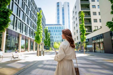Kendine güvenen bir iş kadını elinde dizüstü bilgisayarla iş bölgesinde dolaşıyor. Trençkot giyen orta yaşlı profesyonel bir kadın.