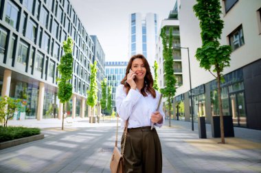 İş yerindeki ofise yürüyen kendine güvenen bir iş kadını. Profesyonel bir kadın cep telefonunu kullanıyor ve iş görüşmesi yapıyor. Esmer, iş kıyafeti giyen bir kadın.. 