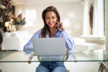 Esmer kadın masada oturuyor ve laptopunu iş için kullanıyor. Evde çalışan ve video konferansı yapan çekici bir kadın. Merkez Ofis. 
