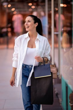 Alışveriş merkezinde yürüyen ve vitrinlere bakan orta yaşlı bir kadın. Sarı saçlı, sıradan kıyafetler giyen bir kadın.. 