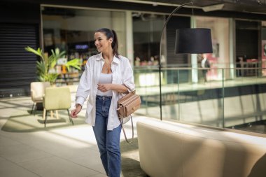 Alışveriş merkezinde yürüyen orta yaşlı bir kadın. Sarı saçlı, sıradan kıyafetler giyen ve neşeli gülümseyen bir kadın.. 