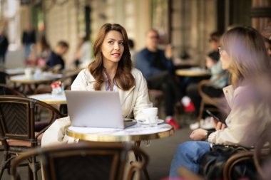 İki orta yaşlı kadın bir kafede terasta oturuyor ve konuşuyorlar. İki bayan arkadaş gündelik kıyafetler giyip kahve içiyorlar.. 