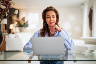 Esmer kadın masada oturuyor ve laptopunu iş için kullanıyor. Evden çalışan çekici bir kadın. Merkez Ofis. 