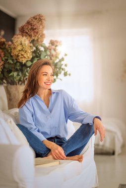 Güzel bir kadın evde rahatlatıcı bir günün tadını çıkarıyor. Orta yaşlı bir kadın, rahat kanepesinde uzanmış kitap okurken ışıl ışıl gülümserdi.. 