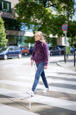 Yaya geçidinden geçen beyaz bastonlu kör kadın portresi. Sıradan kıyafetler giyen ve sopasıyla karşıya geçen görme engelli bir kadın. Tam boy çekim