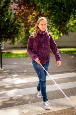 Yaya geçidinden geçen beyaz bastonlu kör kadın portresi. Sıradan kıyafetler giyen ve sopasıyla karşıya geçen görme engelli bir kadın. Tam boy çekim