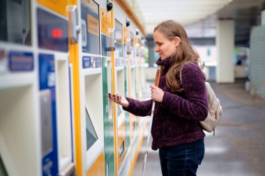 Köpeği olan kör bir kadın tren istasyonundaki makineden bilet alıyor. Kendinden emin bir kadın makinenin önünde duruyor ve ücretsiz ödeme yapıyor..  