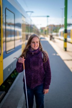 Şehrin dışındaki tren istasyonunda yürüyen beyaz bastonlu kör kadın portresi. Treni bekleyen görme engelli bir kadın. Günlük kıyafetler..  