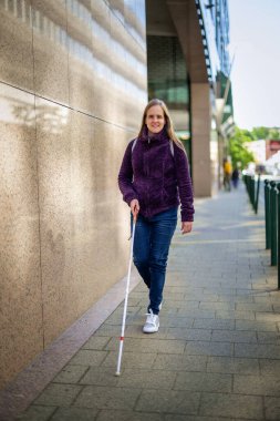 Kendine güveni tam bir kadın portresi, görme engelli, elinde bir baston tutarak şehir sokaklarında yürüyor. Sarı saçlı, sıradan kıyafetler giyen bir kadın.. 