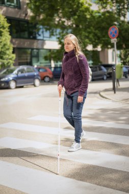 Kendine güvenen bir kadının portresi, görme engelli, yaya geçidinde yürürken elinde kör bir baston tutuyor. Sarı saçlı, sıradan kıyafetler giyen bir kadın.. 