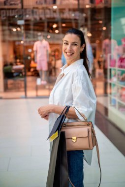 Alışveriş merkezinde yürüyen ve vitrinlere bakan orta yaşlı bir kadın. Sarı saçlı, sıradan kıyafetler giyen bir kadın..  