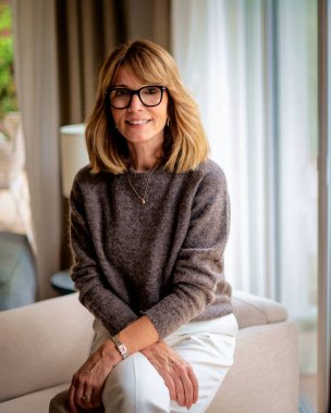 Modern evindeki koltukta oturan sarı saçlı çekici kadının portresi. Orta yaşlı kadın kameraya bakıyor ve gülümsüyor..  