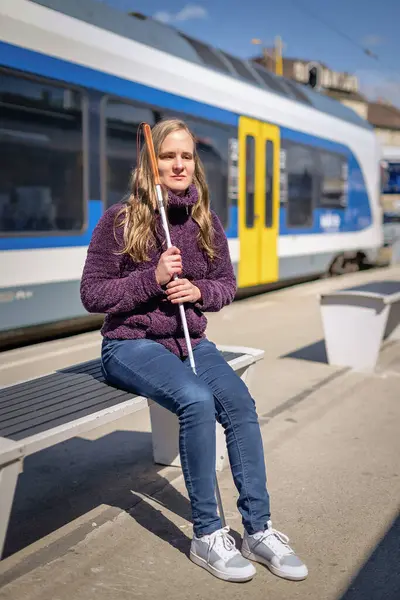 Şehrin dışındaki tren istasyonunda oturan beyaz bastonlu kör kadın portresi. Treni bekleyen görme engelli bir kadın. Günlük kıyafetler. Tam uzunluk.   