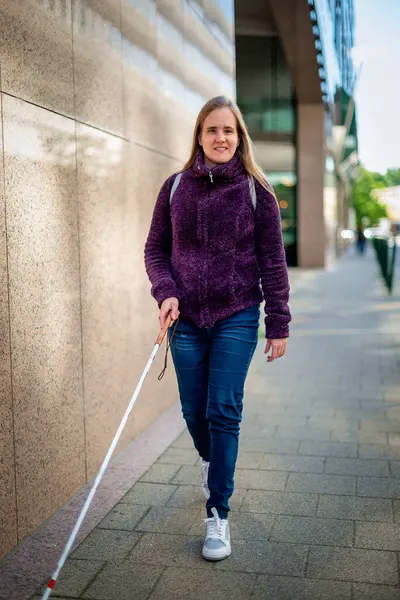 Kendine güveni tam bir kadın portresi, görme engelli, elinde bir baston tutarak şehir sokaklarında yürüyor. Sarı saçlı, sıradan kıyafetler giyen bir kadın.. 