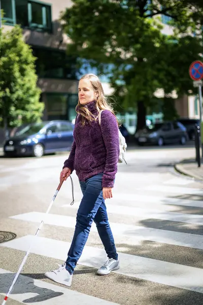 Kendine güvenen bir kadının portresi, görme engelli, yaya geçidinde yürürken elinde kör bir baston tutuyor. Sarı saçlı, sıradan kıyafetler giyen bir kadın.. 