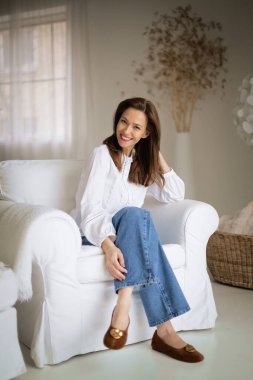 Güzel bir kadın evde rahatlatıcı bir günün tadını çıkarıyor. Rahat koltuğunda otururken gülümseyen orta yaşlı bir kadın..