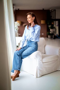 Güzel bir kadın evde rahatlatıcı bir günün tadını çıkarıyor. Rahat koltuğunda otururken gülümseyen orta yaşlı bir kadın..